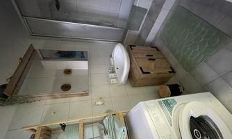 A modern bathroom with a shower, a sink, and a washing machine. There are wooden shelves and green towels that create a relaxing atmosphere.