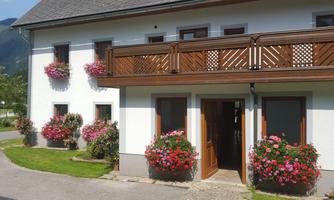 A beautiful house with a wooden balcony and colorful flower baskets. The entrance area is welcoming and well-maintained.