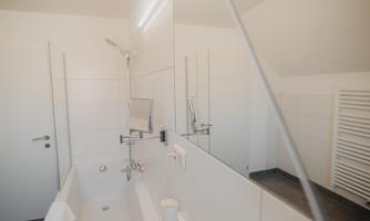 A modern bathroom with a bathtub, mirrors, and bright tiles. The environment is clean and designed in a minimalist style.