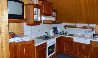 A cozy kitchen with wooden cabinets and a modern stove. In the background, there is an older television and a bright countertop.