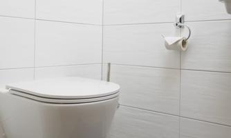 A modern bathroom with a wall-mounted toilet and gray tiles. In front of the toilet is a blue bath mat.