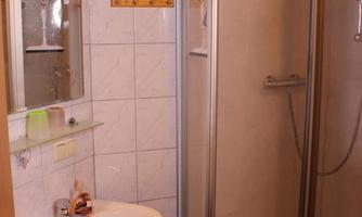 A small bathroom with a shower and a sink. The walls are tiled and there is a mirror as well as some towels.