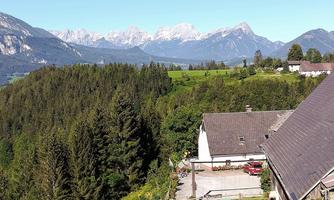 A picturesque landscape with green forests and majestic mountains in the background. Traditional buildings are visible in the foreground.