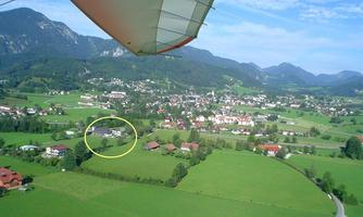 A picturesque landscape with gentle hills and a small town in the valley. In the foreground, there is a green field and some houses.