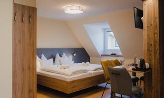 A modern hotel room with a large bed and wooden floor. The room is bright and cozy, with a desk and chairs.