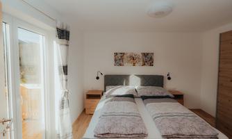 A cozy bedroom with a double bed and modern wooden shelves. Large windows provide plenty of daylight and an inviting atmosphere.