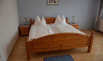 A simple bedroom with a wooden bed and two pillows. Next to the bed are nightstands and a blue mat on the floor.