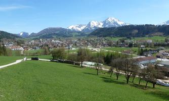 A picturesque landscape with green fields and snow-capped mountains in the background. In the foreground, a small village is visible.