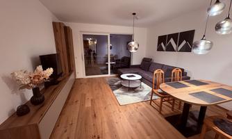A modern living room with a cozy sofa, a round table, and stylish lamps. The room features bright walls and a warm wooden floor.