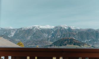 A breathtaking mountain landscape with snow-covered peaks and a clear sky. In the foreground, a wooden railing is visible.