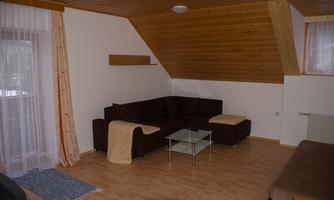 A cozy living room with a dark couch and a glass table. The wood paneling and large windows create an inviting atmosphere.