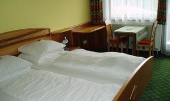 A comfortable hotel room with a large bed and a table. The room has bright walls and a window with curtains.