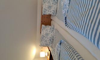 A cozy bedroom with two single beds. The bedding has a blue and white stripe pattern, and a small lamp stands next to the beds.