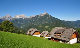 A picturesque landscape with traditional cottages and green meadows. In the background, impressive mountains rise under a clear blue sky.