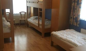 A simple room with two bunk beds and a single bed. Bright walls and large windows create a friendly impression.