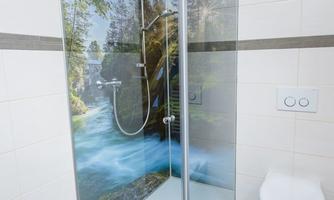 A modern shower with a glass partition and a bright tiled floor. In the background, there is a mural featuring an idyllic landscape.