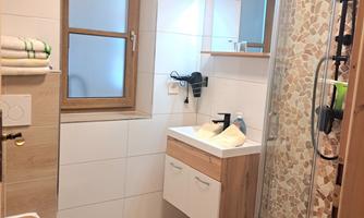 A modern bathroom with a shower and a wooden sink. Bright tiles and a window create a friendly atmosphere.