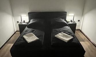 A modern bedroom with a large black upholstered bed. Next to the bed are two nightstands with lamps.