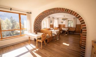 An inviting dining area with wooden chairs and tables. Large windows provide bright light and a view of nature.