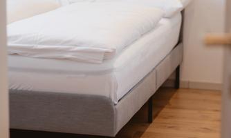 A modern bed with a gray headboard and white bed covers. The floor is wooden, and the room feels friendly and inviting.