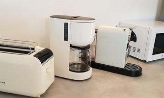 A modern kitchen with white appliances. Among them are a toaster, a coffee machine, an espresso machine, and a microwave.