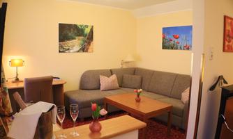 A cozy living room with a gray sofa and a wooden table. Colorful pictures hang on the walls, and the table is decorated with champagne glasses and a vase of flowers.