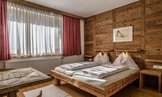 A cozy bedroom with two wooden beds and a warm atmosphere. Large windows provide plenty of daylight and an inviting environment.