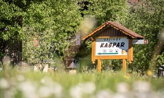 A sign of the inn Kaspar can be seen in front of a green landscape. Surrounded by trees and meadows, the place radiates an inviting character.