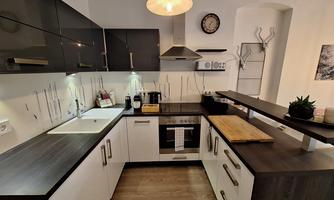 A modern kitchen with elegant black and white cabinets. Equipped with a stove, sink, and wooden countertop.
