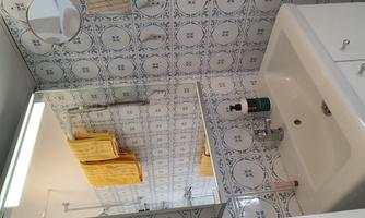 A modern bathroom with a sink and a large mirror. The walls are adorned with blue tiles, and two yellow towels hang on the wall.