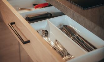 An opened kitchen drawer with cutlery and kitchen utensils. The drawer has a light wood surface and an organized arrangement.