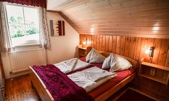 A cozy bedroom with wooden paneling and a double bed. The window offers a view of the greenery and the room is well-lit.