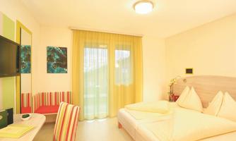 A bright room with two beds and large windows. There is a desk, a television, and colorful decorative elements.