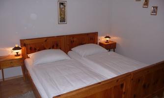 A cozy bedroom with a wooden double bed and two nightstands. The walls are painted light and decorated with some pictures.
