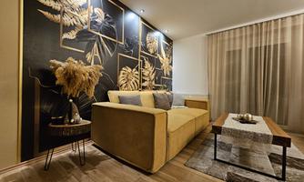 A modern living room with a yellow sofa and an elegant wall design. Decorative elements are on the table and next to the sofa is a stylish side table.