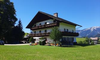 A large, beautiful country house with balconies and a well-kept garden. In the background, green meadows and mountains can be seen.