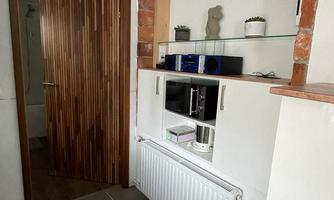 A modern hallway with a wooden door and an integrated shelf. On the shelf are plants and various devices.
