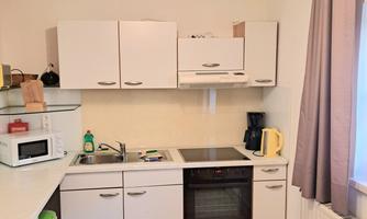 A modern kitchen with white cabinets and a stove. Various kitchen appliances and utensils are visible on the countertop.