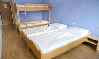 A simple bedroom with a bunk bed and two single beds. The walls are painted blue, and the floor is made of light wood.
