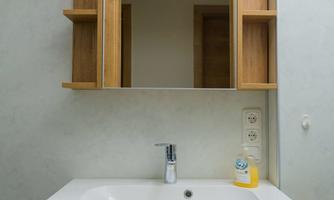 A modern sink with a wooden cabinet underneath and a mirror above it. The room is designed simply and brightly.