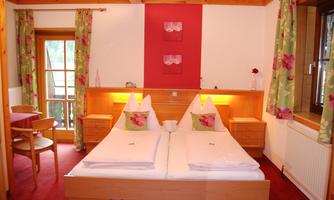 A cozy bedroom with a double bed and colorful curtains. The reddish walls and wooden interior create an inviting atmosphere.