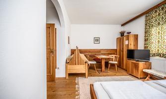 A cozy room with wooden furniture and a television. There is a small table with chairs and large windows that let in light.
