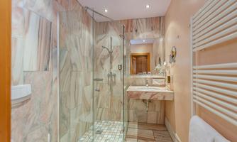 A modern bathroom with a glass shower cubicle and elegant marble tiles. The walls and floor are in soft color tones, featuring a sink and stylish fixtures.