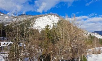 A winter landscape with snow-covered hills and trees. The sky is blue with some clouds.