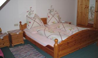 A cozy bedroom with a wooden bed and two large pillows. Next to it are nightstands and a wooden wardrobe.