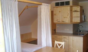 A cozy room with wooden furniture and a small kitchenette. On the left side, there is a bed that is separated by curtains.