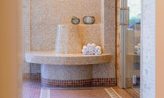 An elegant wellness bath with mosaic walls and a round seating area. Freshly folded towels are ready to create a relaxing atmosphere.
