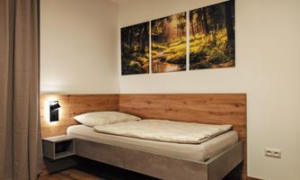 A simple bedroom with a single bed and a wood look. Pictures of a forest hang on the wall, creating a calm atmosphere.