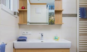 A modern bathroom with a sink and a wooden cabinet. The walls are bright, and a mirror above reflects the light.