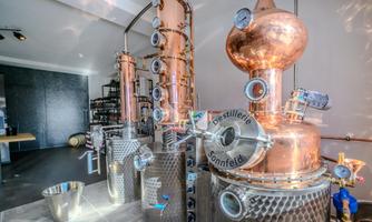 A modern distillery with copper distillation equipment. The room is bright and clearly structured, with some shelves in the background.
